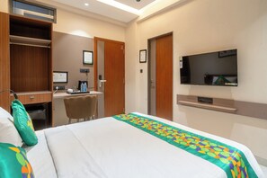 A hotel room with a bed, a desk, a chair, a television, and a wardrobe. - Treebo Hub (Indore)