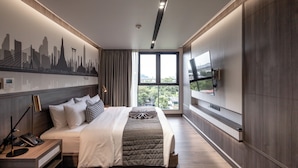 Une chambre d’hôtel moderne dotée d’un grand lit, d’une fresque représentant un paysage urbain, d’une télévision et offrant une vue sur l’extérieur.