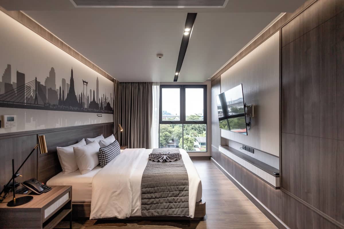 A modern hotel room with a large bed, a cityscape mural, a TV, and a view of the outdoors.