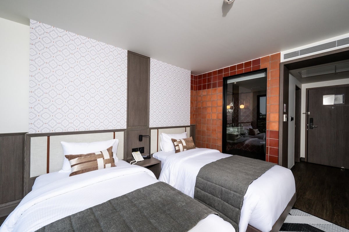 A hotel room with two beds, a nightstand, a telephone, and a door leading to a bathroom.