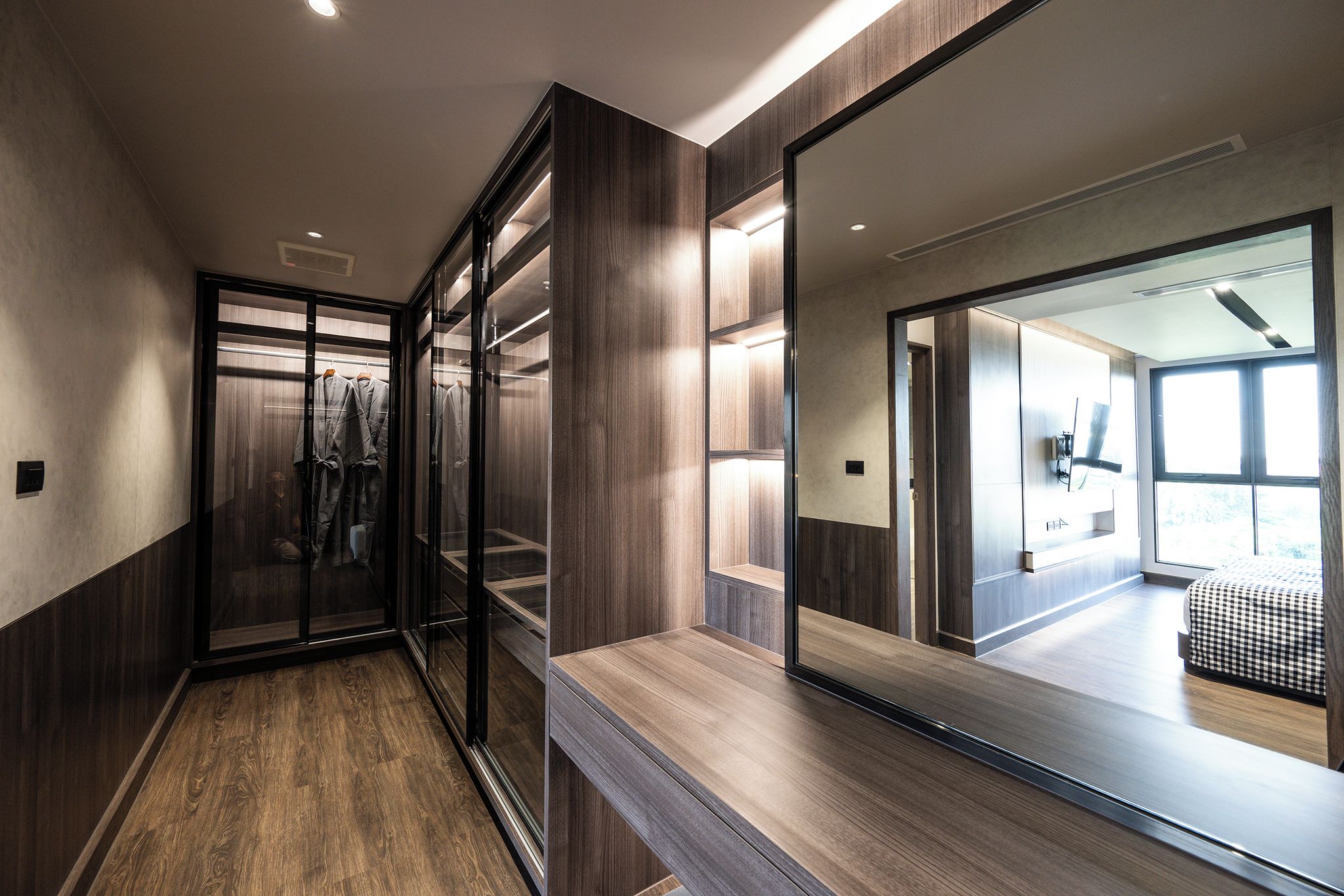 A modern hotel room with a large mirror, wooden flooring, and a view of the adjacent room.