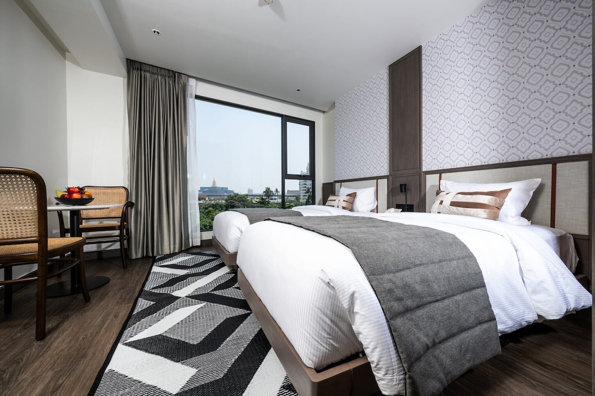 A hotel room with a large bed, a dining area with a table and chairs, and a view of the cityscape through a large window.