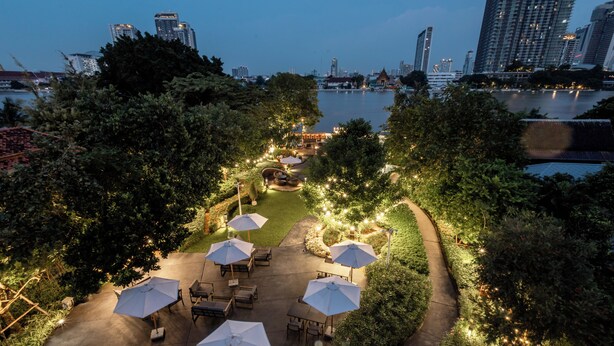 Une terrasse extérieure avec des tables et des parasols, entourée d’arbres et offrant une vue sur les bâtiments d’une ville.