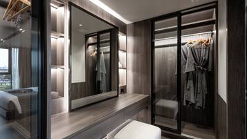 A modern bathroom with a large mirror, a vanity, and a walk-in closet with hanging clothes.