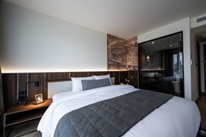 A modern hotel room with a large bed, a wooden headboard, a bedside table with a lamp, and a large mirror. - We Hotel Riverfront (Bangkok)