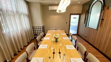 A conference room with a long table, chairs, a vase with flowers, and a large window with curtains.