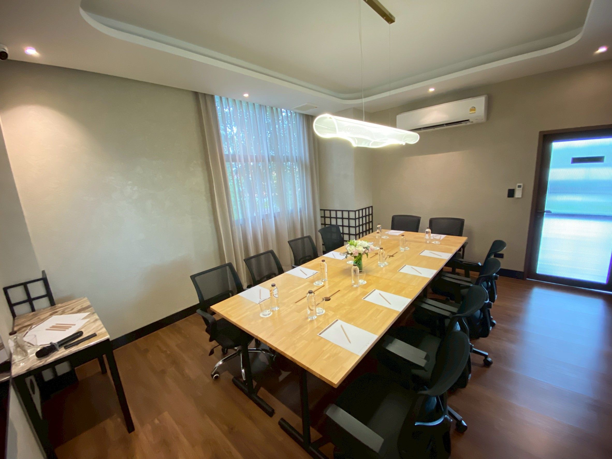Una sala de conferencias con una larga mesa, sillas y una mesita auxiliar con una botella y vasos.