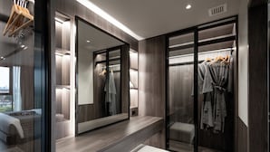 Une salle de bain moderne avec un grand miroir, un meuble-lavabo et un dressing où les vêtements sont suspendus.
