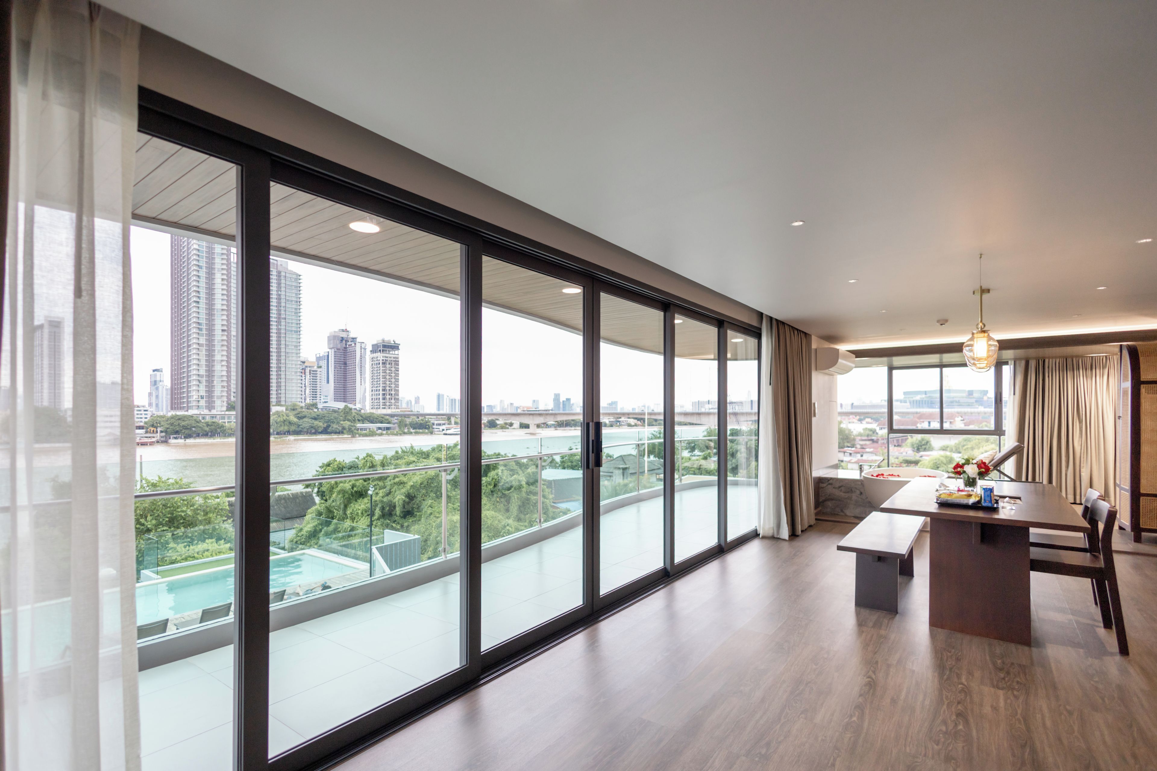 A modern interior with large windows, a dining area, and a view of a river and cityscape.