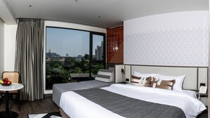 A hotel room with a bed, a small table with fruit, a view of the city, and a large window with curtains. - We Hotel Riverfront (Bangkok)