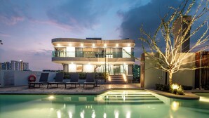 Ein modernes Gebäude mit Pool, Liegestühlen und gut beleuchteter Fassade.