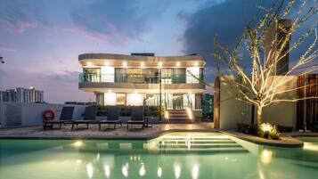 Un bâtiment moderne doté d’une piscine, de chaises longues et d’un éclairage extérieur soigné.