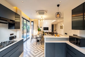 A modern kitchen with a central island, built-in appliances, and a dining area with a view. - Staymaster Villa Novara - 3BHK  (Vagator)