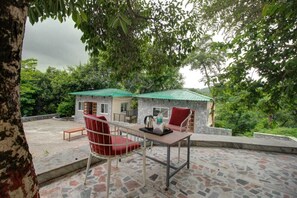 Un patio con mesa y sillas, suelo de piedra y vista a un edificio con techo verde.