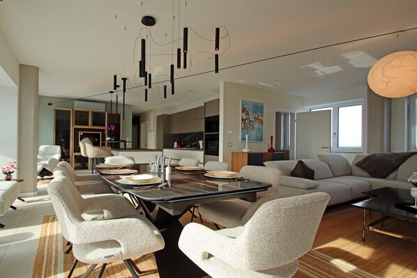 A modern living room with a dining area, featuring a large table, comfortable seating, and contemporary lighting fixtures.