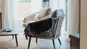 Una silla de mimbre con un cojín oscuro en una habitación luminosa con vistas a la vegetación.