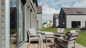 Una terraza con mobiliario exterior y una puerta de vidrio que da a un área techada.