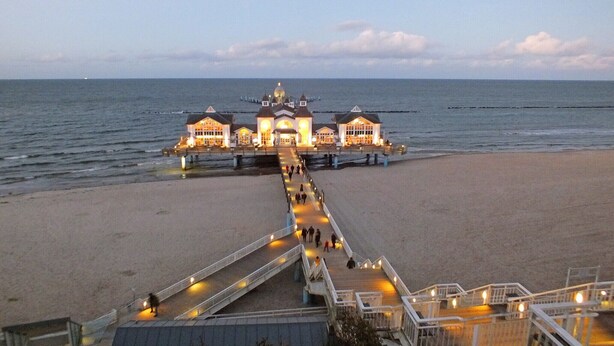 Un muelle que lleva a un edificio con cúpula, una playa y vistas al mar.