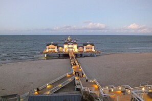 Eine Steg, der zu einem Gebäude mit einer Kuppel, einem Strand und einem Blick aufs Meer führt.