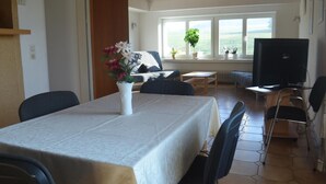 A dining area with a table set for four, a sofa, a TV, and a view of the outdoors. - Ferienwohnung für neun Personen in Homberg (Homberg)