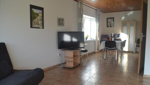 A living room with a TV, a sofa, a dining area with chairs, and a kitchen in the background. - Ferienwohnung für neun Personen in Homberg (Homberg)