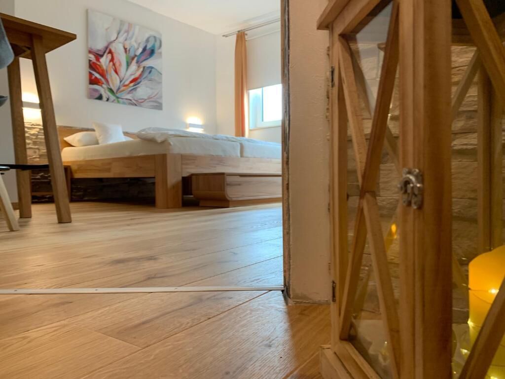 Un dormitorio con cama, piso de madera, un cuadro en la pared y una ventana con cortinas.