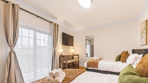 Quarto de hotel com duas camas, uma escrivaninha, um espelho e vista da cidade através de grandes janelas.
