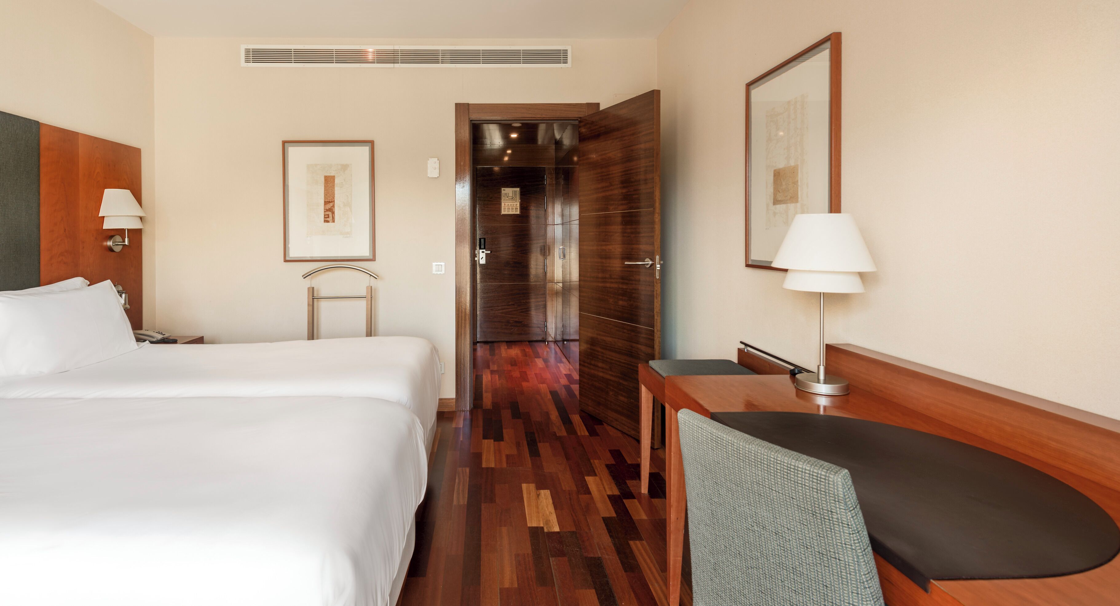 Une chambre d’hôtel avec un grand lit, un bureau avec une chaise, une lampe et un tableau encadré au mur.