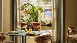 A dining area with a table set for two, a chair, and a view of a room with a sofa and a plant. - Nh Marbella (Marbella)