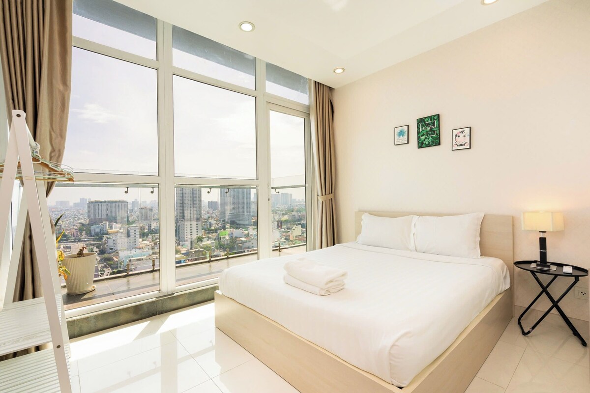 Ein Hotelzimmer mit einem großen Bett, Blick auf die Stadt und einem kleinen Tisch mit einer Lampe.