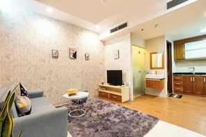 Ein modernes Wohnzimmer mit einem grauen Sofa, einem kleinen Couchtisch und einem Flachbildfernseher. Es gibt eine Küchenzeile mit Holzausstattung und einem Spülbecken.