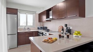 Ett modernt kök med ett Bosch-kylskåp, en mikrovågsugn, en kaffemaskin och en skärbräda i trä, dekorerad med frukt och bakverk.