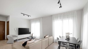 Ett modernt vardagsrum med en soffa, ett matbord med stolar, en platt-TV och en taklampa.