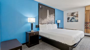A hotel room with a large bed, two bedside tables, a nightstand, a wall-mounted lamp, and a painting.