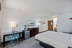 A hotel room with a bed, desk, chair, and a small kitchenette.