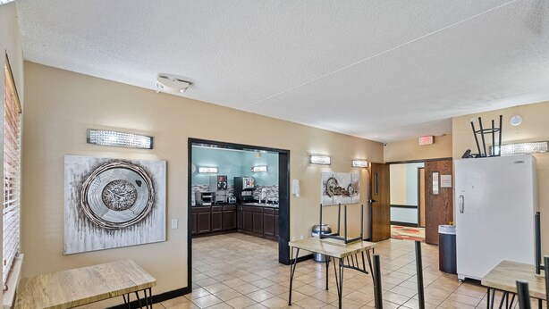 A hotel room with a kitchenette, a dining area with a table and chairs, and a large abstract painting on the wall. - Woodland Inn & Suites Extended Stay - 1 King Bed Non Smoking (Wichita)