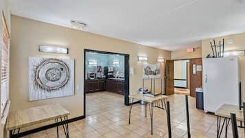 A hotel room with a kitchenette, a dining area with a table and chairs, and a large abstract painting on the wall.