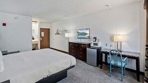 A hotel room with a bed, desk, chair, microwave, and a painting on the wall.
