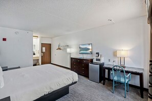 A hotel room with a bed, desk, chair, microwave, and a painting on the wall.
