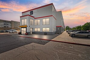 A multi-story building with a red and white color scheme, large windows, and a parking lot with cars.