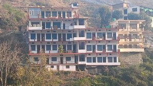 A multi-story building with balconies, located in a hilly area.