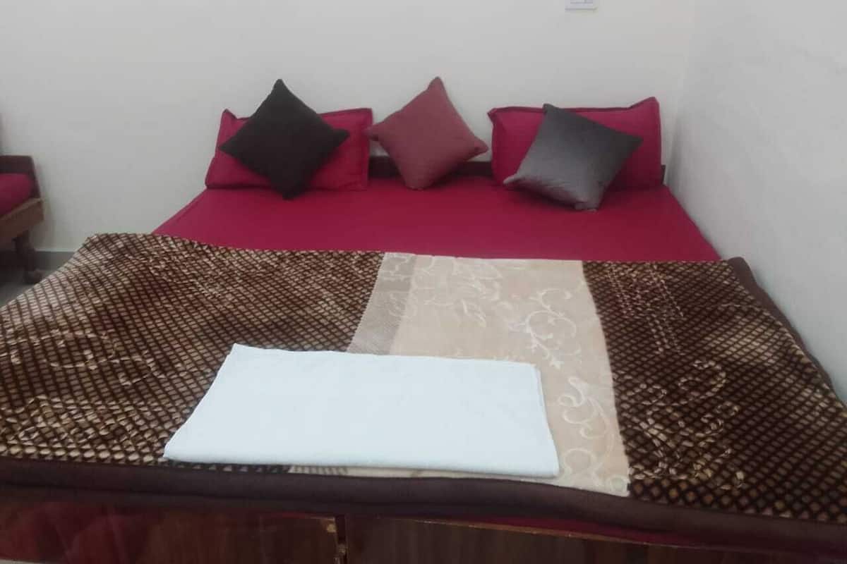 Cama com colcha vermelha e várias almofadas em cores diferentes.