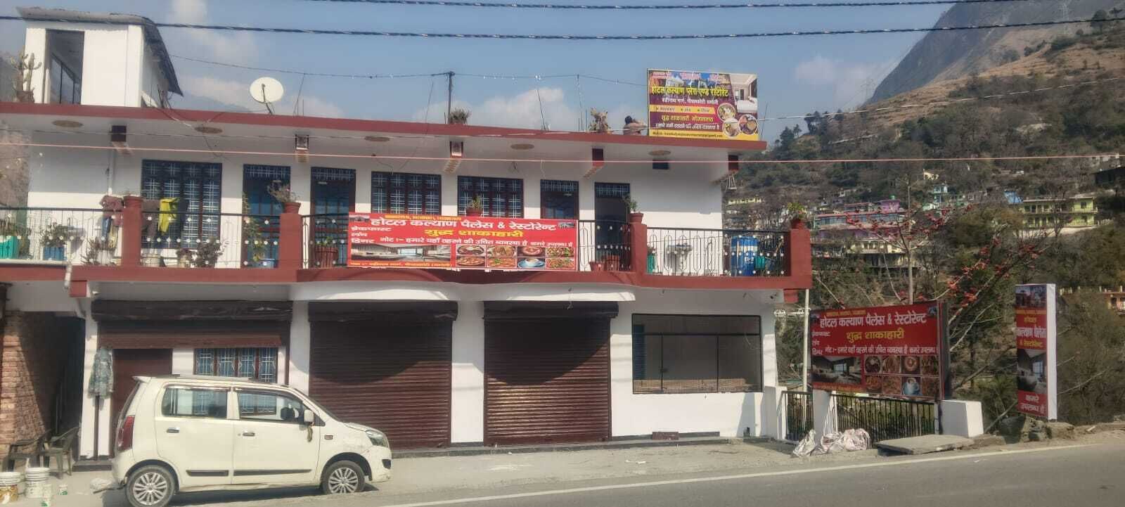 Un immeuble de deux étages doté d’un balcon, une voiture garée et plusieurs panneaux publicitaires pour des services de restauration.