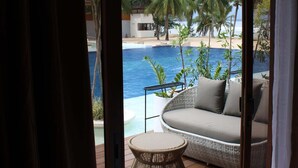 A room with a large sliding glass door leading to a poolside area with a wicker sofa and a round table. - Dahican Beach Resort and Spa (Mati)