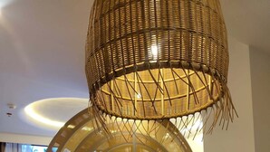 A modern dining area with a round wooden table, a white vase with dried flowers, and a large woven light fixture above. - Dahican Beach Resort and Spa (Mati)