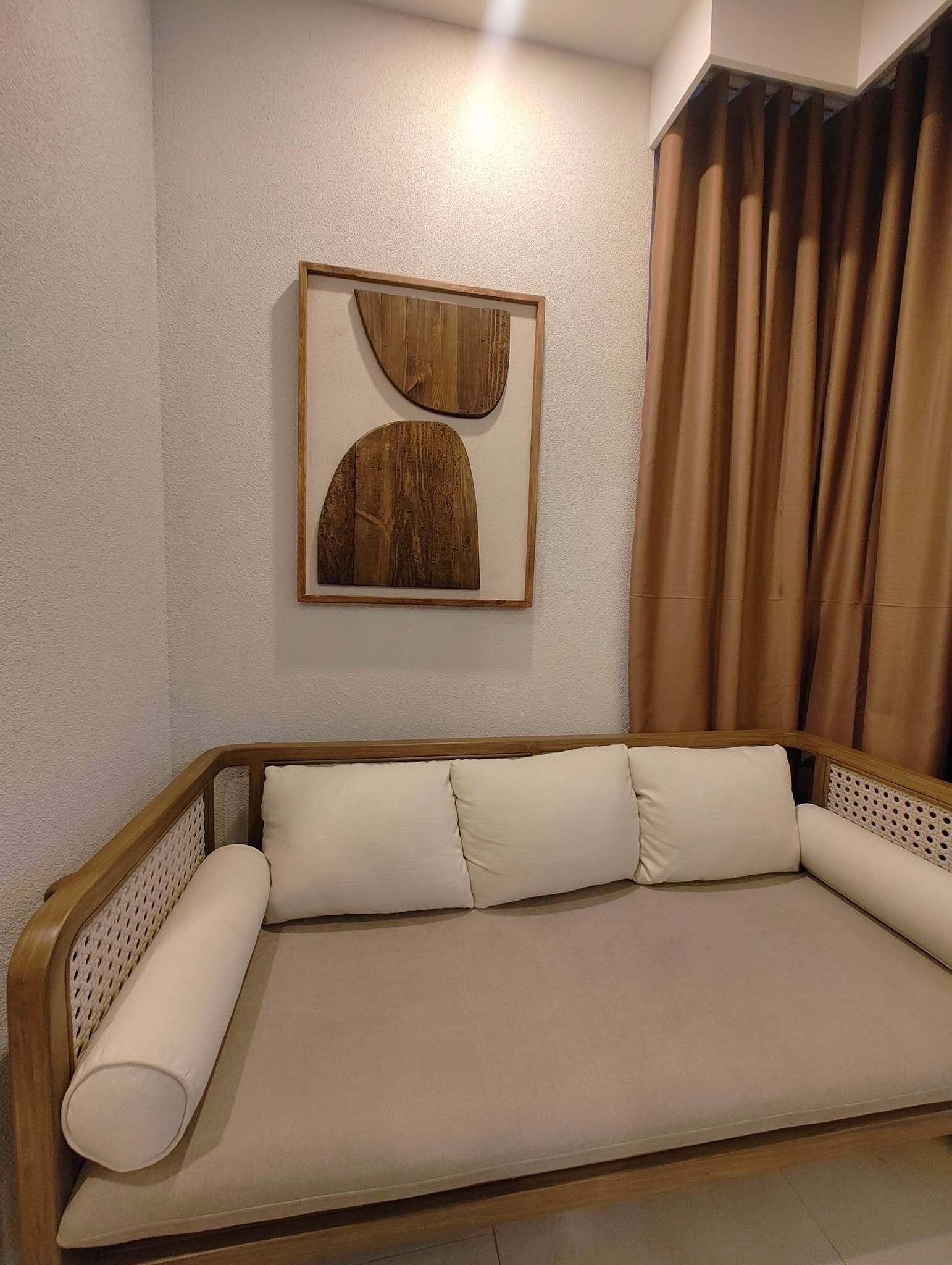 A sofa with a wooden frame and beige cushions, a wooden wall art piece, and a brown curtain.