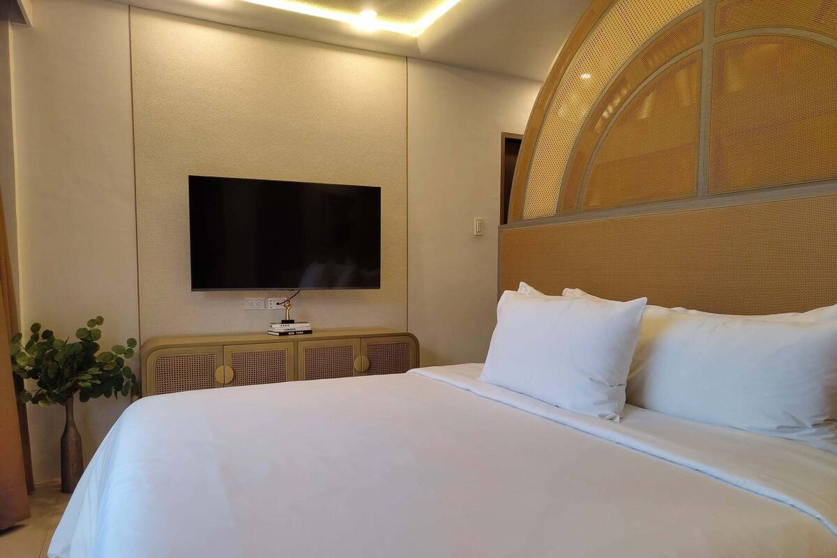 Una habitación de hotel moderna con una cama grande, un televisor de pantalla plana en la pared y un cabecero decorativo.