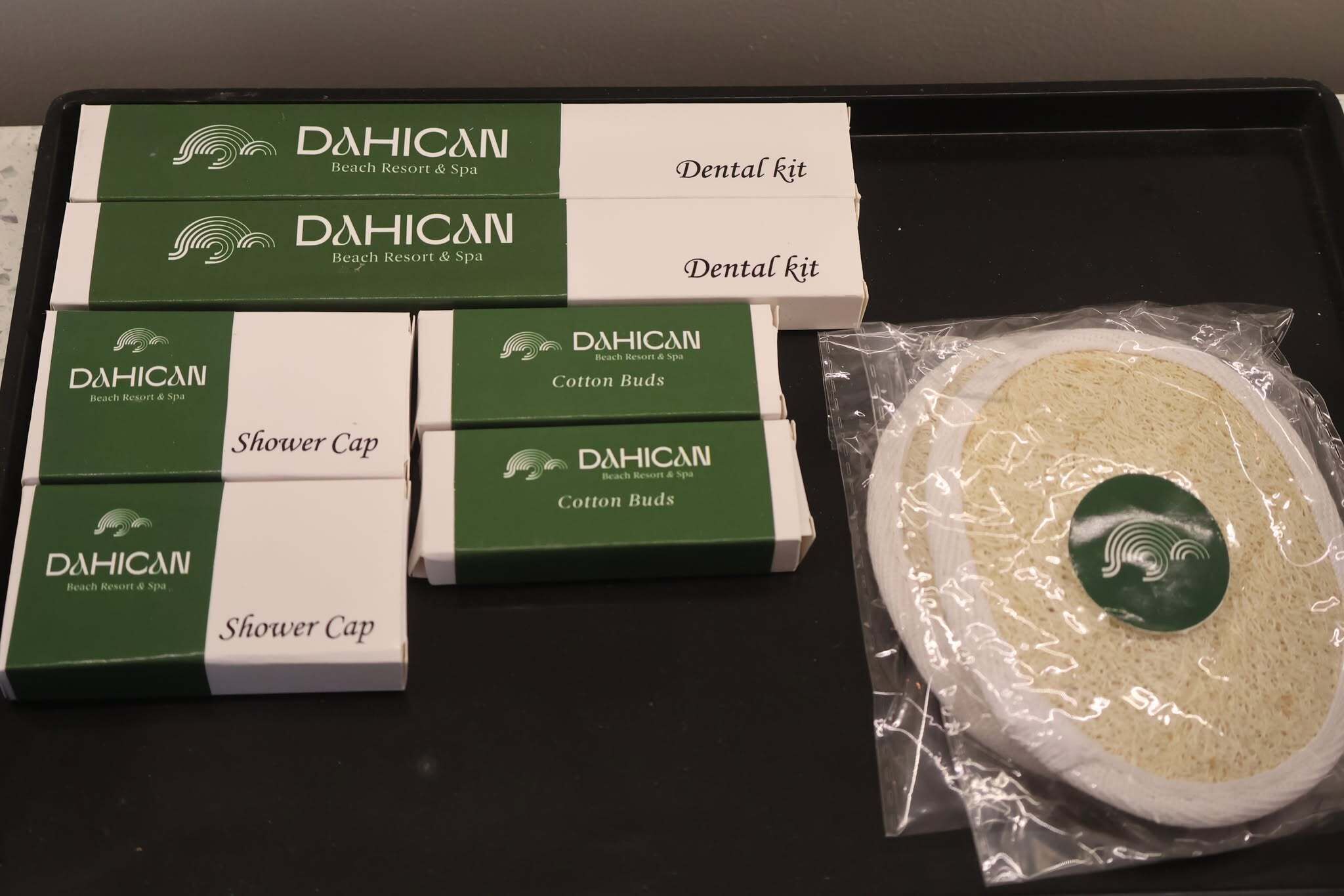 A tray with various DAHICAN Beach Resort & Spa products including dental kits, shower caps, and cotton buds.