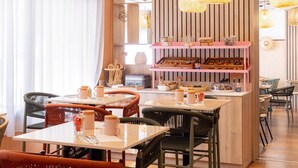 A cozy café with wicker chairs, a central table with coffee cups, and a pink shelf with pastries. - Mercure Nice Centre Notre Dame Hotel (Nice)