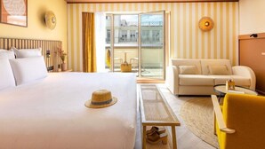 A hotel room with a bed, a sofa, a small table, a chair, a balcony with a view, and a wall-mounted light fixture. - Mercure Nice Centre Notre Dame Hotel (Nice)